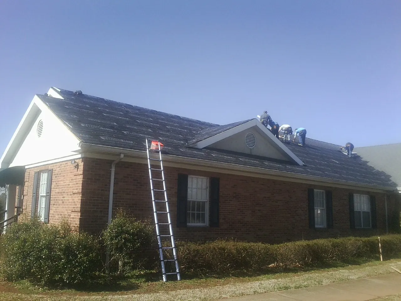 Crew tearing shingles off a brick ranch roof with a ladder set — Emergency Roof Repair work by our crew in Bedminster