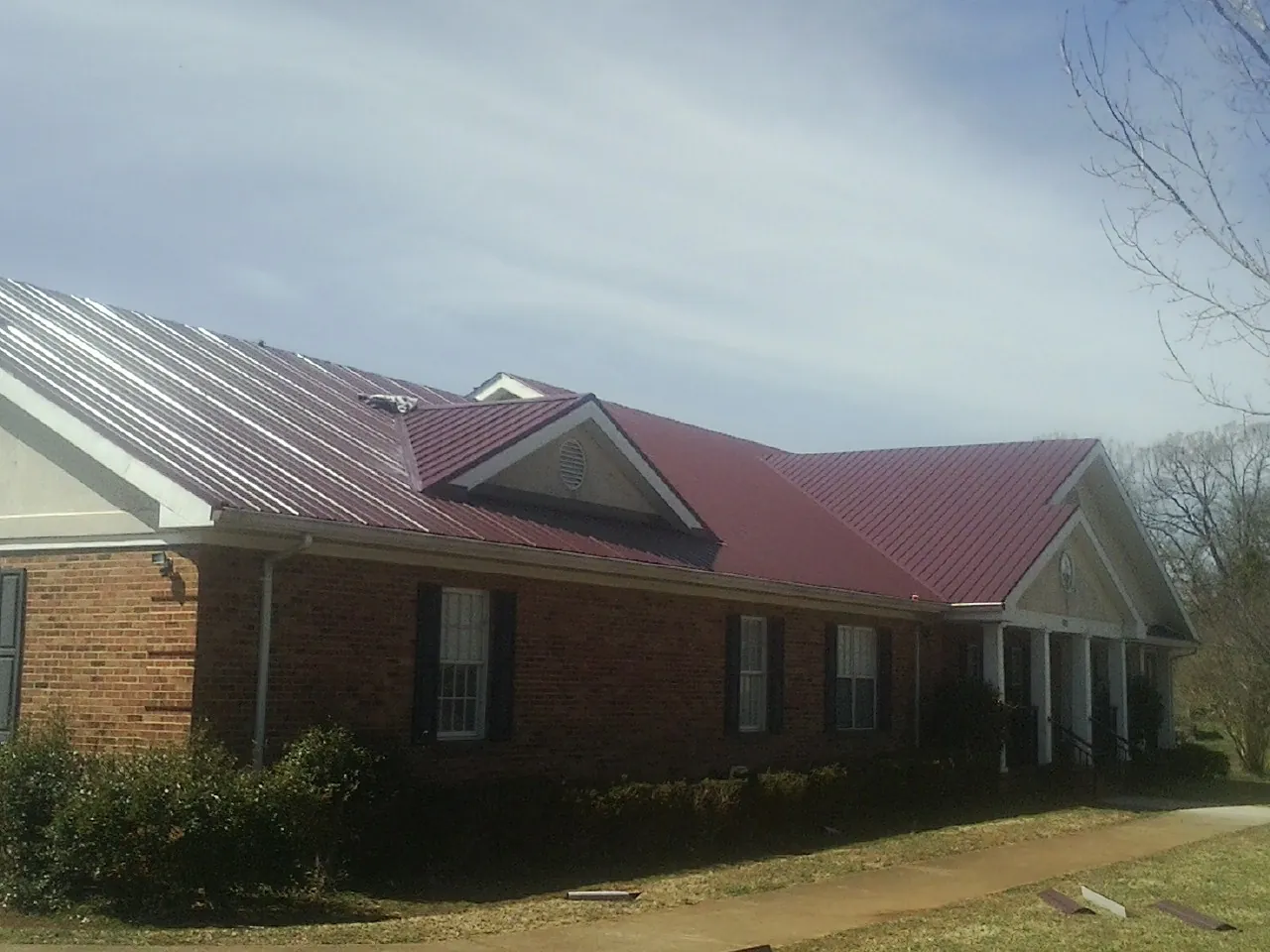 Red metal roof with gabled entries on a long brick building, from a Hail Damage Roof Repair job in Bedminster