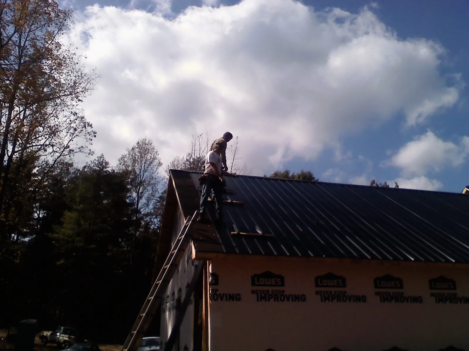 Roofer fastening dark metal panels high against a cloudy sky, from a Roof Inspection job in Bedminster